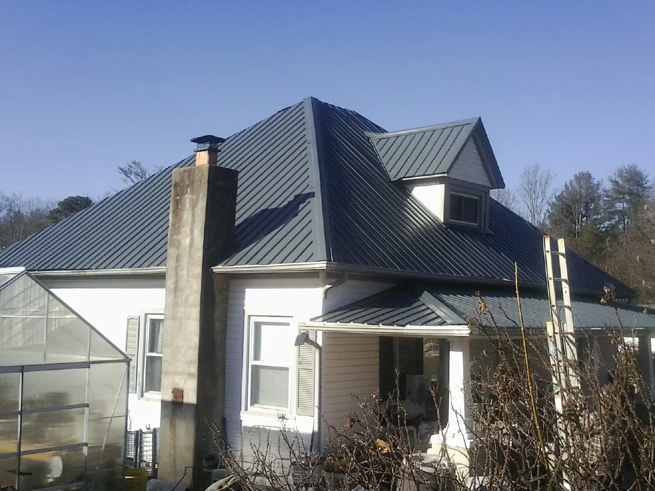 Dark blue standing seam metal roof on a white farmhouse with dormer — Slate & Tile Roof Repair by Roofing Brothers in East Sandwich