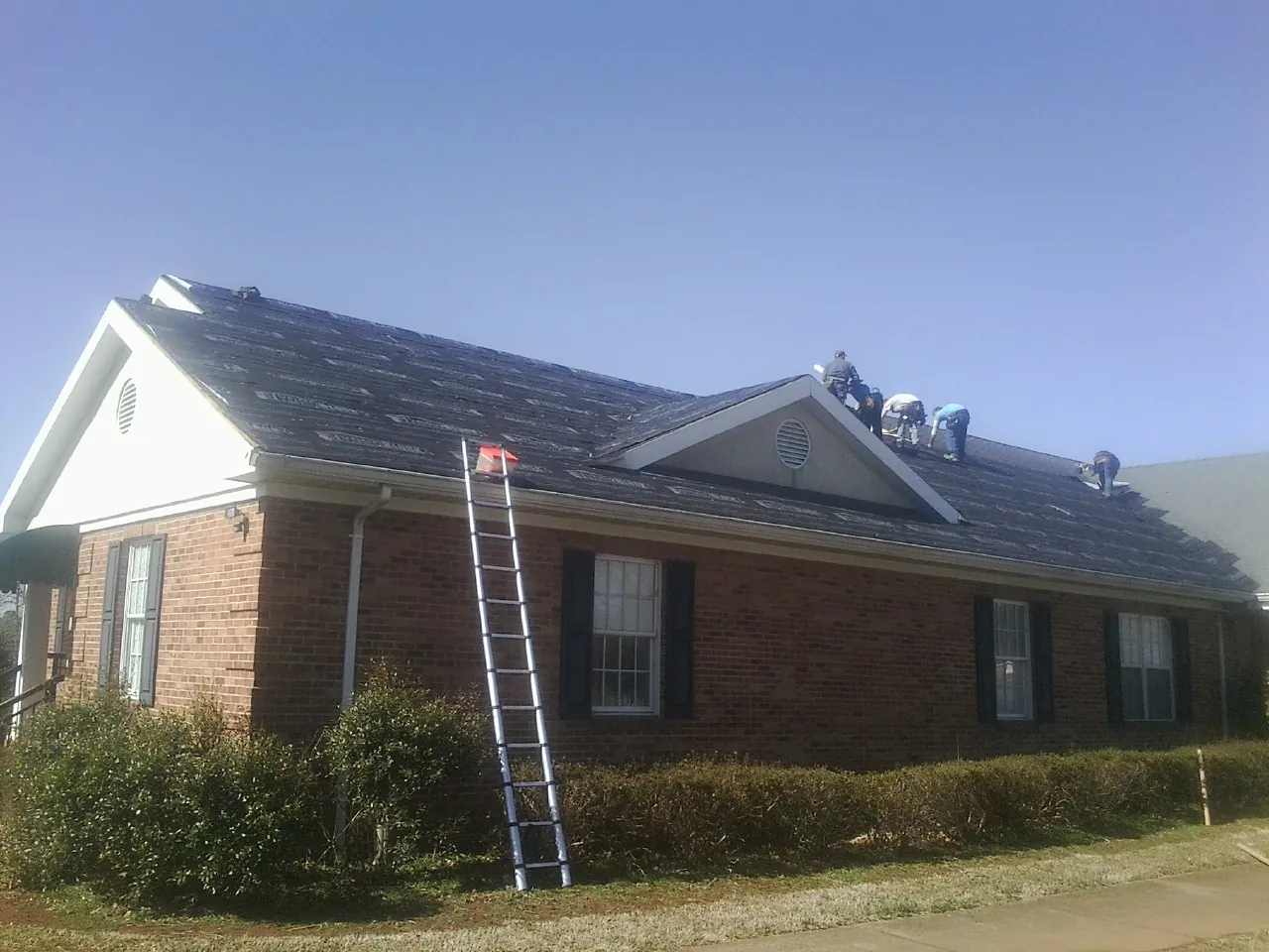 Crew tearing shingles off a brick ranch roof with a ladder set — Emergency Roof Repair work by our crew in East Sandwich