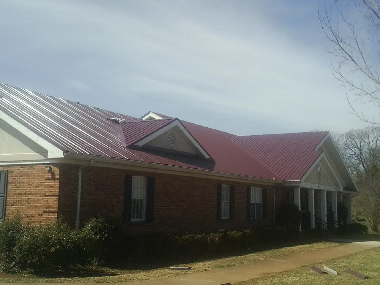 Red metal roof with gabled entries on a long brick building, from a Hail Damage Roof Repair job in East Sandwich