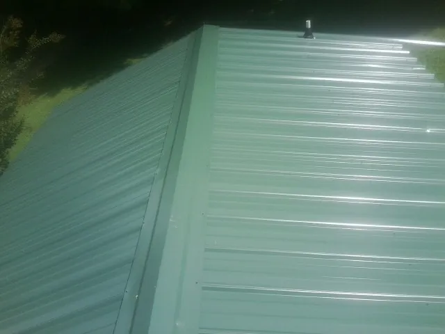 New green metal panels meeting at the ridge of a roof — Flat Roof Repair work by our crew in East Sandwich