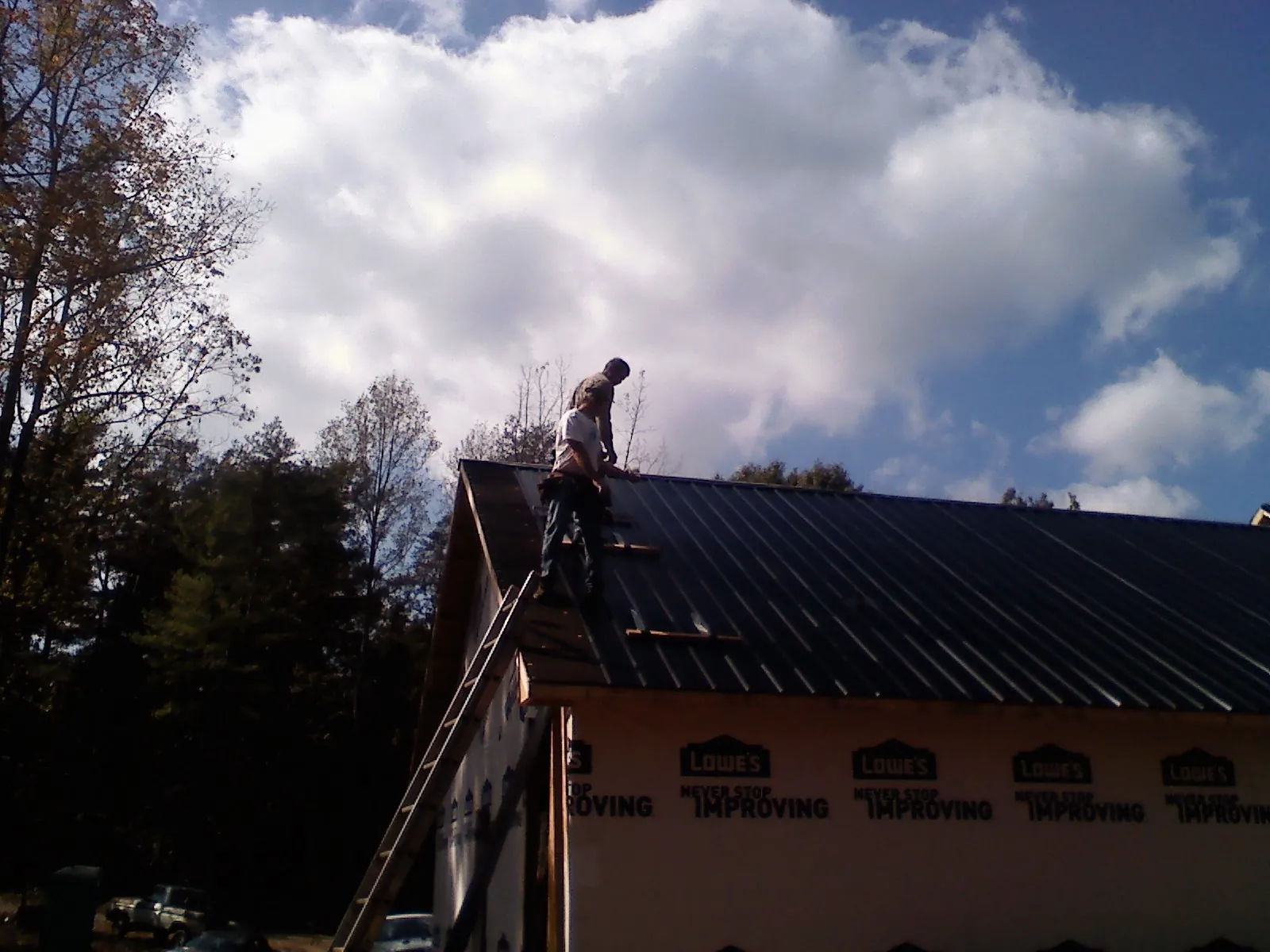Roofer fastening dark metal panels high against a cloudy sky, from a Roof Inspection job in East Sandwich