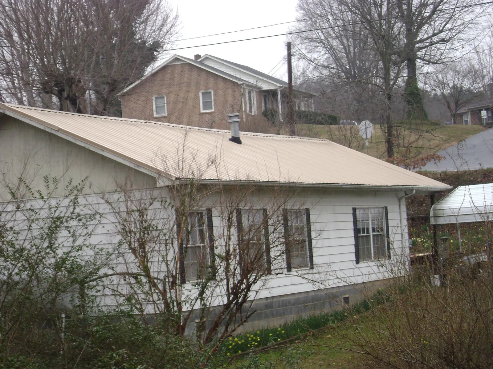 Tan metal roof on a white sided house set into a hillside — Commercial Roofing by Roofing Brothers in East Sandwich